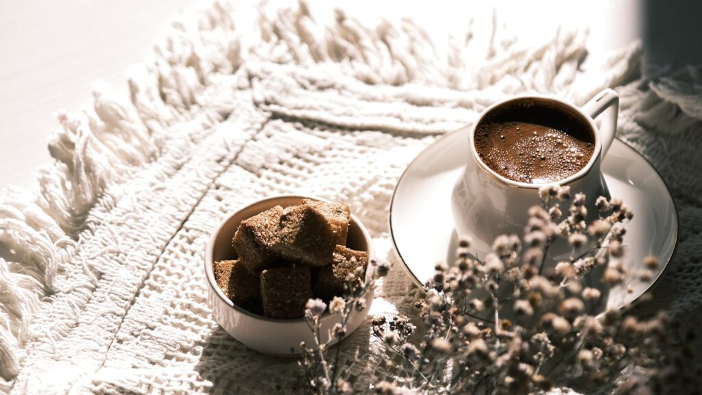 Warm coffee cup and sugar cubes on a textured mat in natural lighting.